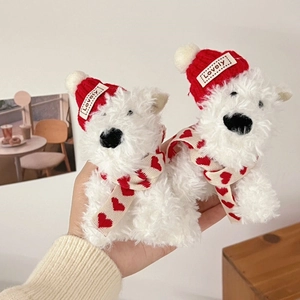 Close-up of white plush puppies wearing red knitted hats and scarves held in hand