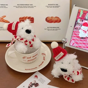 Detailed plush West Highland dog keychain wearing a red hat and scarf on a warm desk