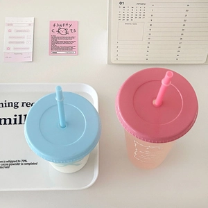 Overhead view of two pastel plastic tumblers with straws on a clean white desk setting