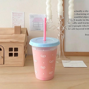 Detail of pink straw cup with blue lid and bow pattern against a cozy decor background