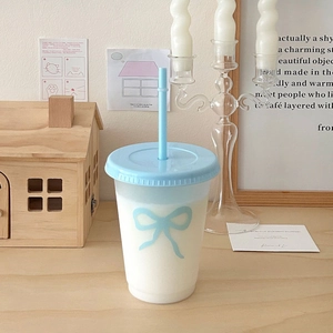 Detail of light blue frosted plastic straw cup with a decorative bow on a wooden table
