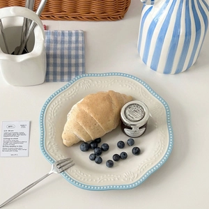 Embossed ceramic dinner plate with blue wavy edges showcasing a croissant breakfast setup