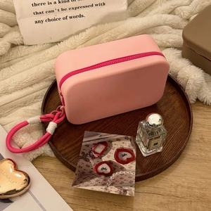 Pink silicone makeup bag on wooden tray with travel toiletries and zip closure detail