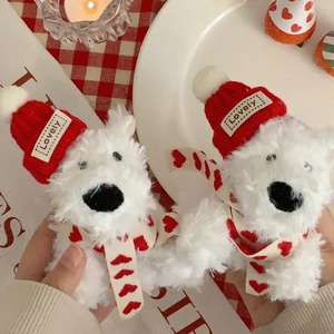 Close-up of white plush bear keychains with red knit hats and heart scarves in a cozy setting