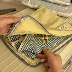 Pale yellow waterproof nylon travel organizer bag being packed into a silver suitcase