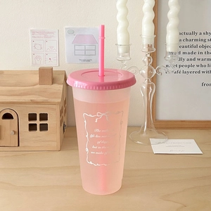 Pink frosted plastic straw cup on a wooden table with aesthetic home decor background