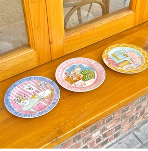 Detailed view of three ceramic plates with hand-painted cat illustrations on a wooden sill