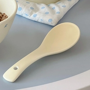 Close-up of a creamy ceramic soup spoon with a round shape and hanging hole on handle