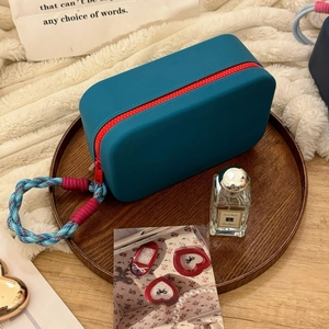 Detail of teal silicone makeup bag with red zipper and woven handle on a wood tray