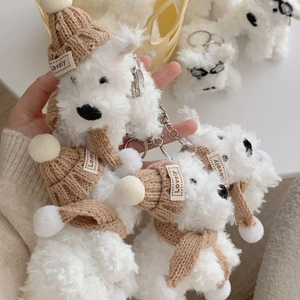 Close-up of white plush dog keychain wearing a brown knit hat and scarf with Lovely label