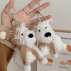 Close-up of white plush dog keychain wearing a brown knit hat and matching scarf