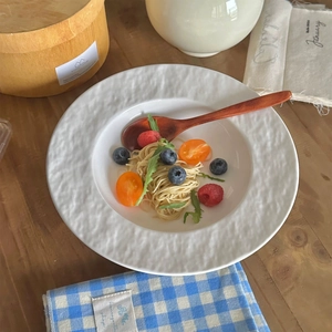 Minimalist white ceramic pasta plate with hammered texture and wood spoon on wood table