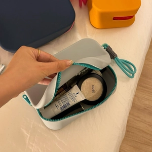 Open detail of a large grey silicone makeup bag with blue zipper and hand strap