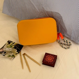Close-up of orange silicone makeup bag with colorful woven handle on white bedding