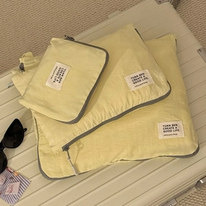 Three-piece set of light yellow travel organizers stacked on a suitcase with sunglasses