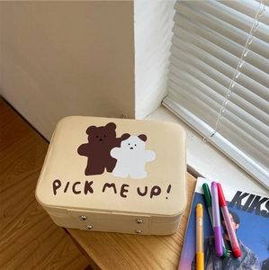 Close-up of cream cartoon bear makeup case with metal accents on a wooden desk