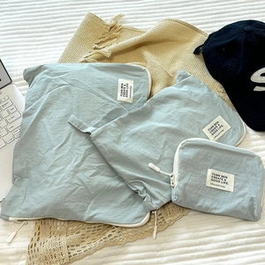 Three light blue nylon travel storage bags in different sizes on a white striped bedsheet
