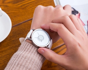 Close-up of modern quartz watch with white leather strap on female wrist with coffee cup