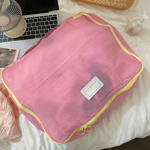 Pink travel mesh organizer bag with yellow zipper on white bedding scene