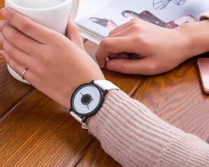 Close-up of a minimalist watch with white leather strap on a wooden desk setting