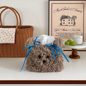 Plush brown bear tissue box cover with blue satin bows in a cozy home setting
