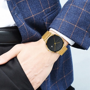 Detailed close-up of a men's business watch with gold mesh strap and black calendar dial