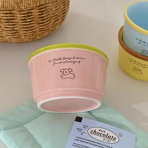 Detail of pink ceramic bowl with green rim and cute puppy illustration in a cozy setting