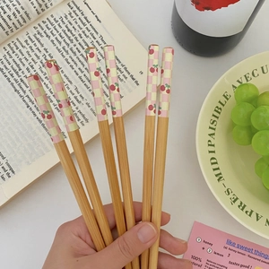 Three pairs of bamboo chopsticks with pink plaid and red cherry patterns in hand