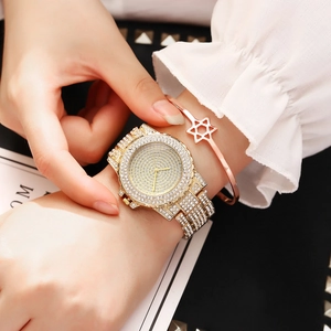 Close-up of luxury gold iced-out watch with matching star bangle on woman wrist