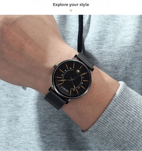 Detail of minimalist black quartz watch with mesh strap on wrist in casual setting