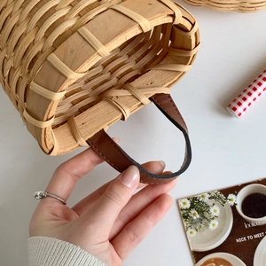 Detail of hand-woven wood storage basket featuring brown leather handles and rivets