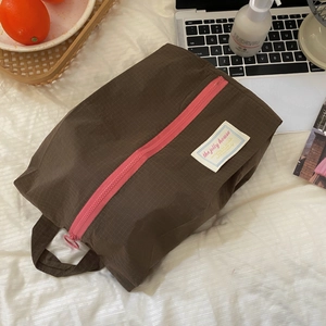 Brown mesh travel organizer bag with pink zipper on white textured bedding closeup