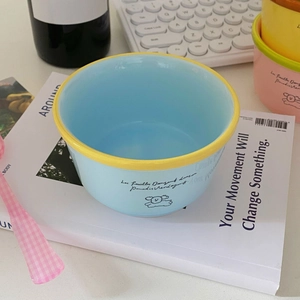 Close-up of a blue ceramic dog bowl with yellow rim on a cozy desk setup