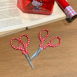 Detail of red polka dot stainless steel scissors on a rustic wooden desk with stationery