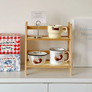 Detail of a 2-tier cream rattan desktop rack featuring light wood and ceramic cups