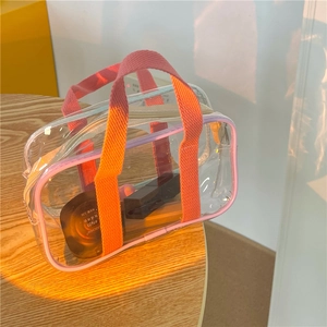 Detail of transparent PVC beach bag with pink nylon handles and cosmetics inside
