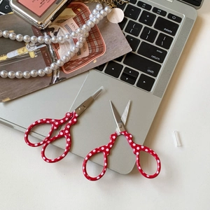 Detail of red polka dot stainless steel scissors with protective cap on laptop