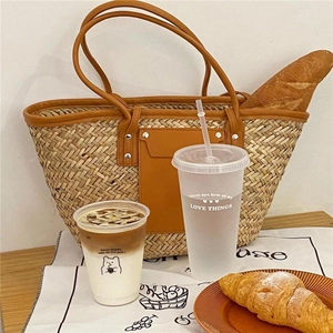 Detail of straw woven tote bag with brown leather pockets and metal rivet accents
