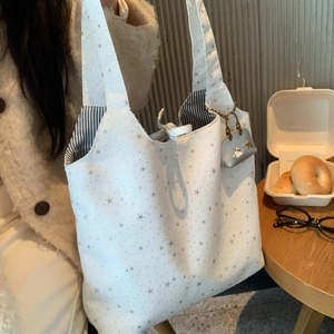 Detail of star pattern white tote bag with striped lining and silver kitty charm accessory