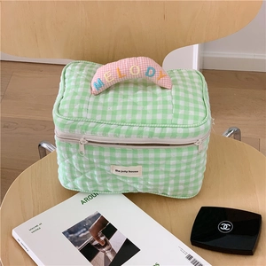 Green gingham quilted cosmetic bag with pink Melody handle on a wooden chair