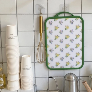 Close-up of vintage floral cutting board with green border hanging on a tiled kitchen wall