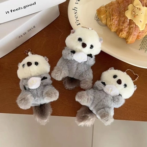 Detailed view of three cute plush sea otter charms with pearl chains on a wooden table