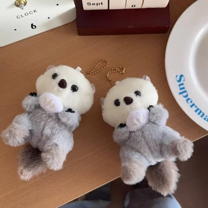 Close-up of plush sea otter charms with soft fur and golden keychains on a desk
