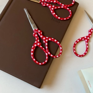 Three red polka dot stainless steel scissors for embroidery and crafts on a notebook
