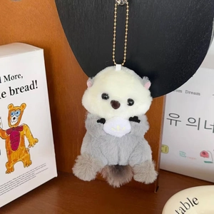Detail of plush sea otter keychain with soft grey fur holding a white shell accessory