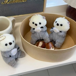 Close-up of three plush sea otter charms with gold chains and soft grey and white faux fur