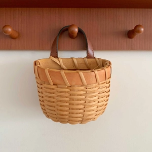 Detail of hand-woven wall-hanging basket with leather handle on wood hook