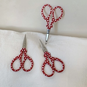 Close-up of red polka dot handle embroidery scissors on white linen background