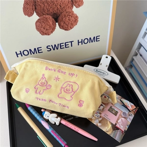 Close-up of bright yellow canvas pencil case with cute cartoon embroidery and slogans