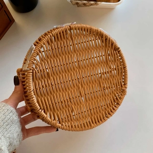 Detailed close-up of woven rattan fruit basket with handles held in hand for scale